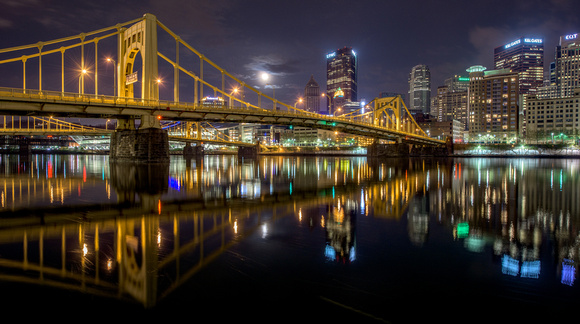 A full moon emerges from the clouds over the Andy Warhol Bridge