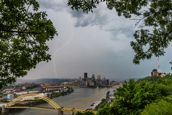 Trees frame Pittsburgh as lightning strikes behind the city