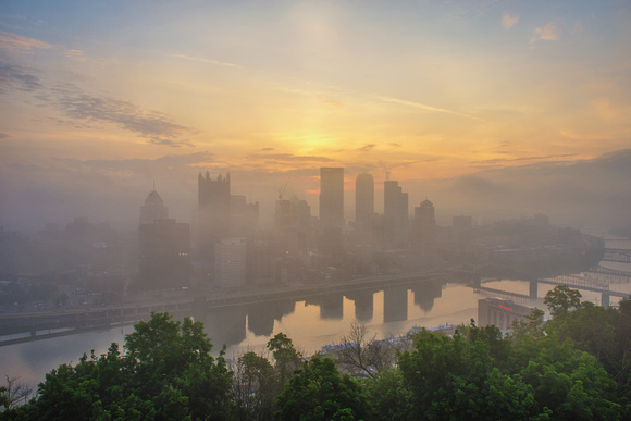 The sun shines through a foggy Pittsburgh skyline from Mt. Washington
