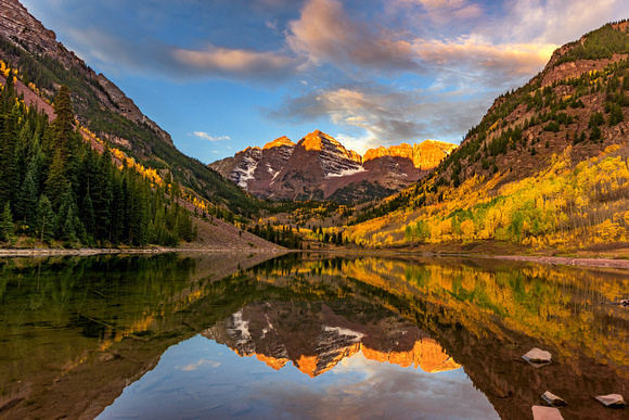 Maroon Bells glows at dawn surrounded by beautiful fall color in Colorado