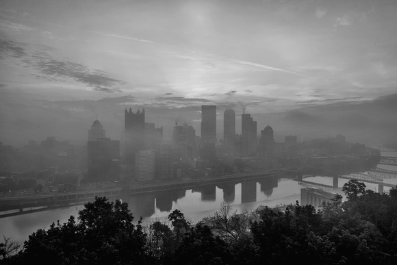 The sun shines through a foggy Pittsburgh skyline from Mt. Washington B&W