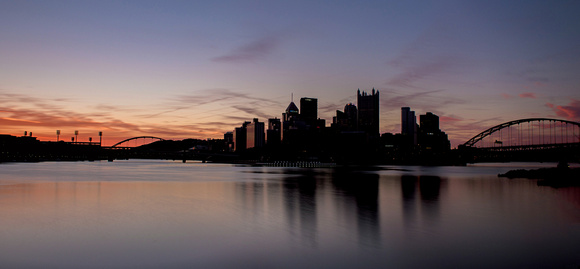 The Pittsburgh skyline is silhouetted against a beautiful morning sky