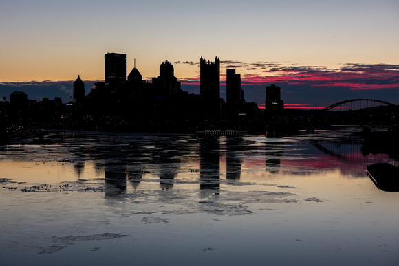 Pittsburgh skyline is silhouetted against a colorful sky