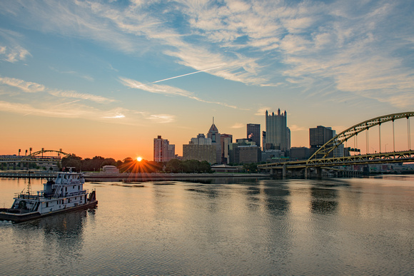 A tow boat sitson the Monongahela River in Pittsburgh un front of a beautiful sunrise