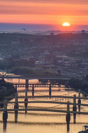 The sun rises behind the clouds at dawn above the Allegheny River in Pittsburgh