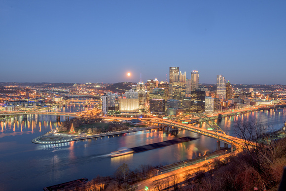 A barge passes by the full moon and PIttsburgh skyline at dusk