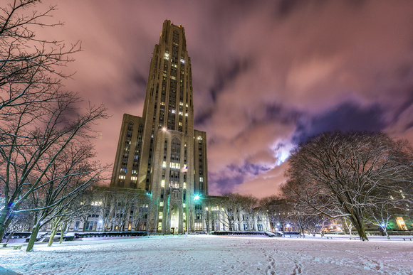 The moon shines through the clouds by the Cathedral of Learning in the snow