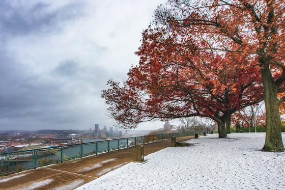 Bright red leaves fill a tree over a snow covered West End Overlook in Pittsburgh