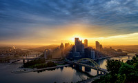 The sun shines through the Pittsburgh skyline at dawn