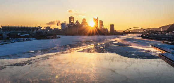The sun bursts through the Pittsburgh skyline over the icy Ohio River