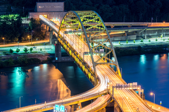 Cars streak over the Ft. Pitt Bridge at night from the Pittsburgh rooftops