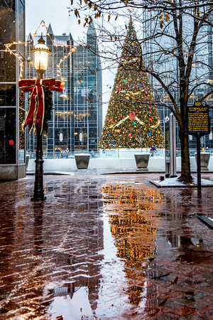 The Christmas tree at PPG Place reflects in the wet sidewalk during a snowstorm in Pittsburgh